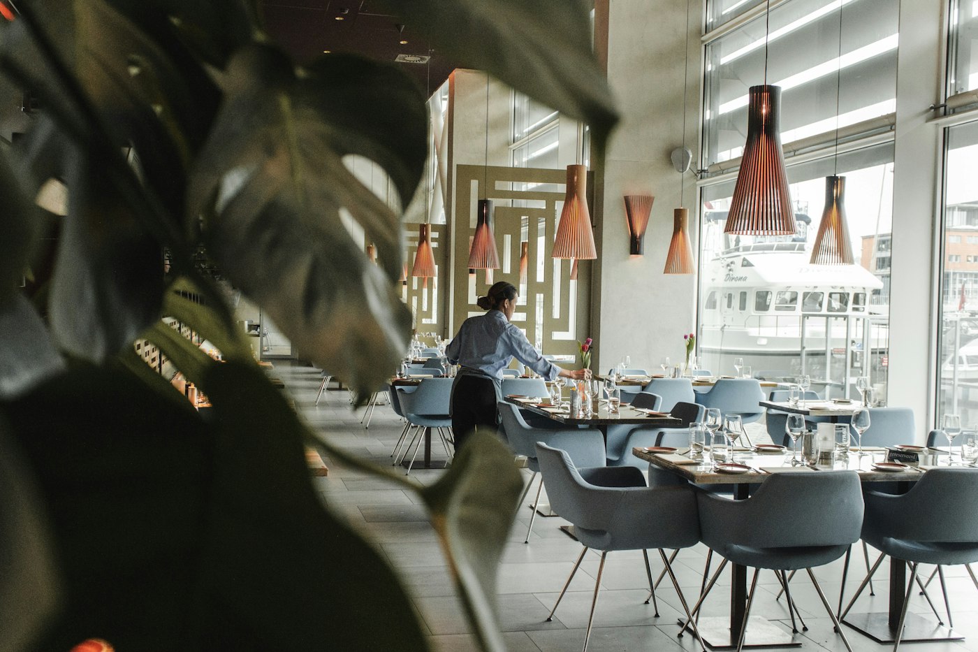 A member of staff preparing an elegant, modern restaurant dining room for service.